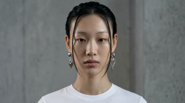 A portrait with slicked-back hair and drop earrings against concrete